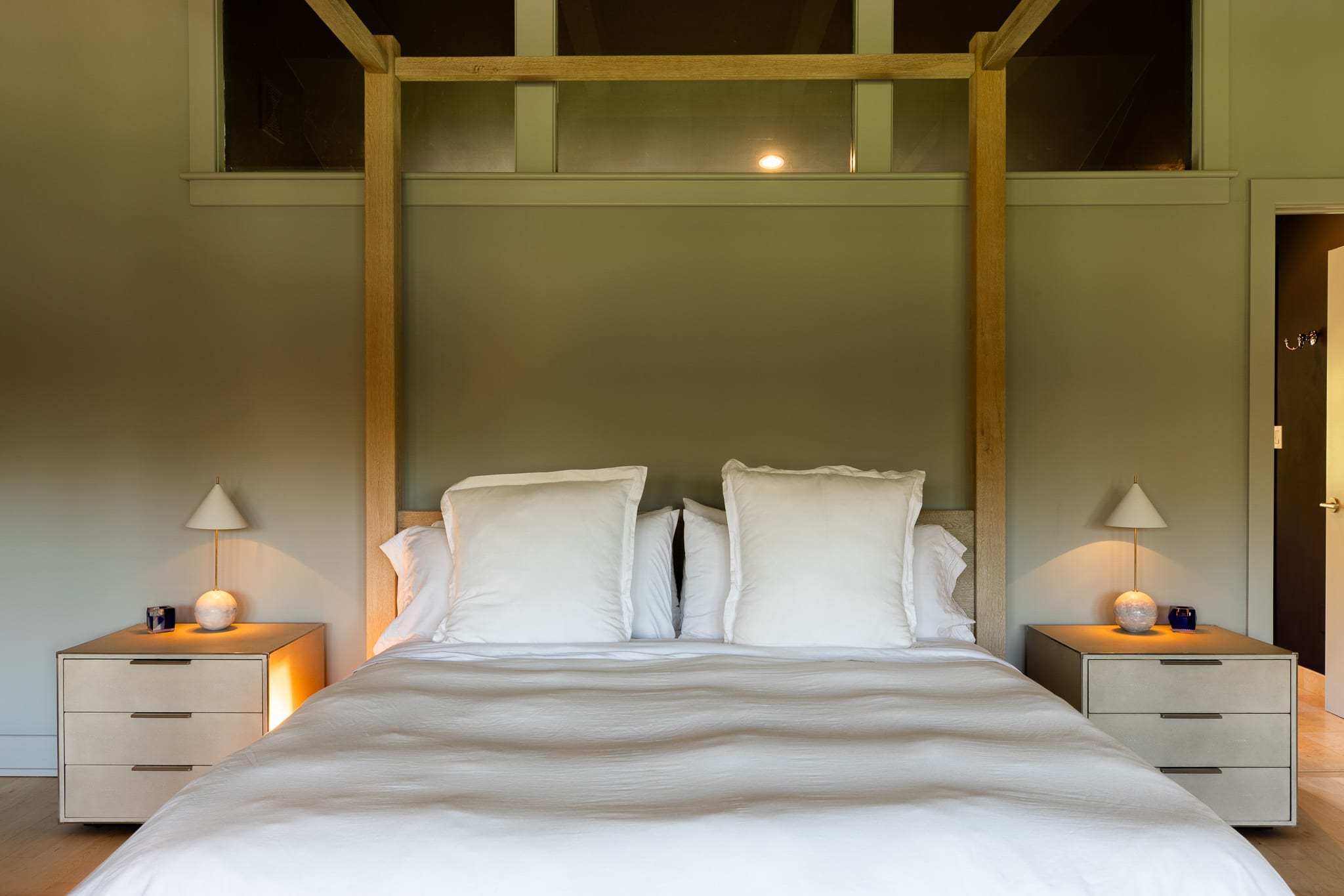Close-up view of the four-poster bed in bedroom-1, featuring white linens and pillows. Two modern nightstands with small lamps are on either side, against a muted green wall.