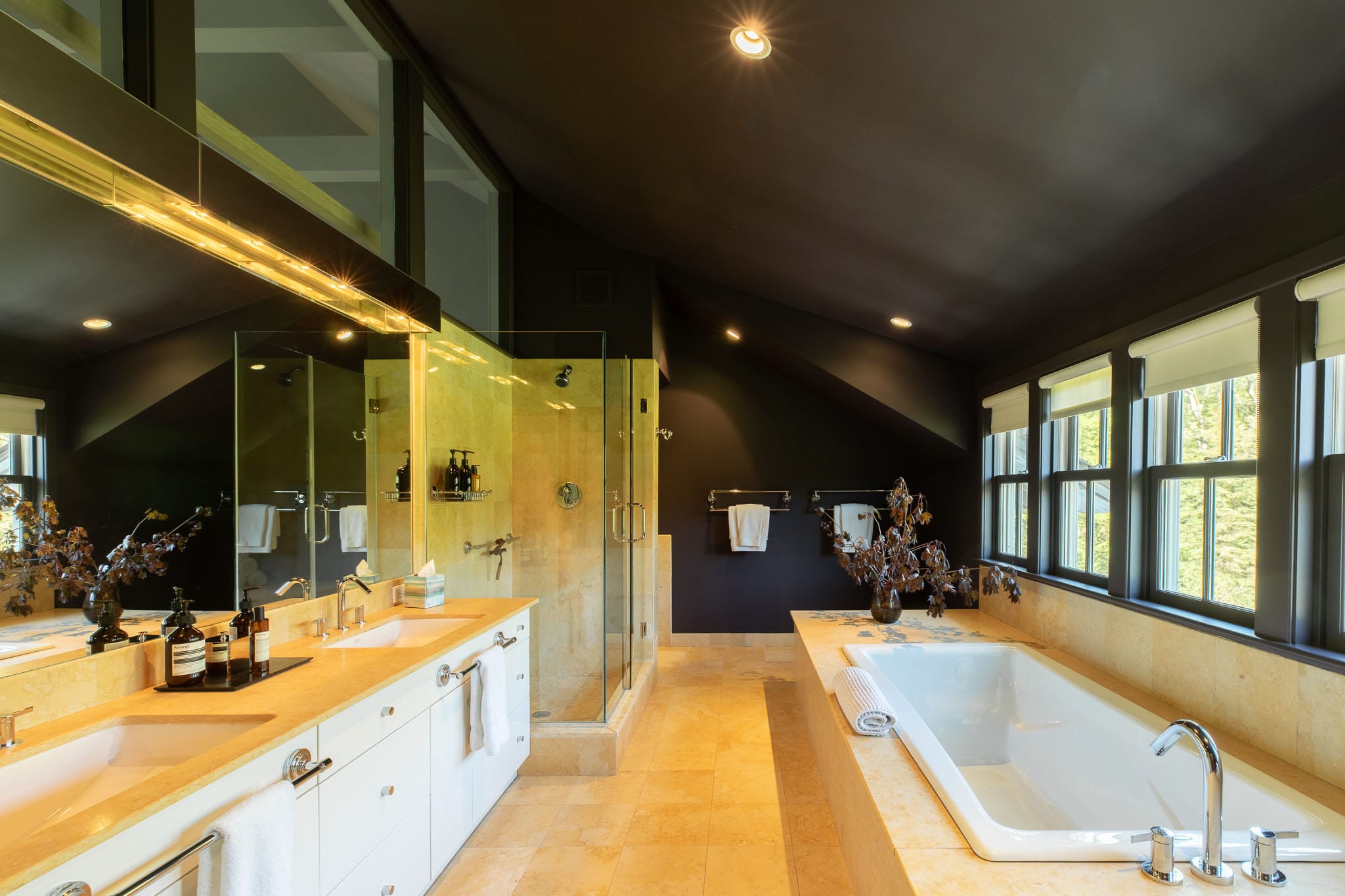 Luxurious bathroom with dark walls and ceiling, featuring a large built-in bathtub, a double vanity with light countertops, and a glass-enclosed shower.