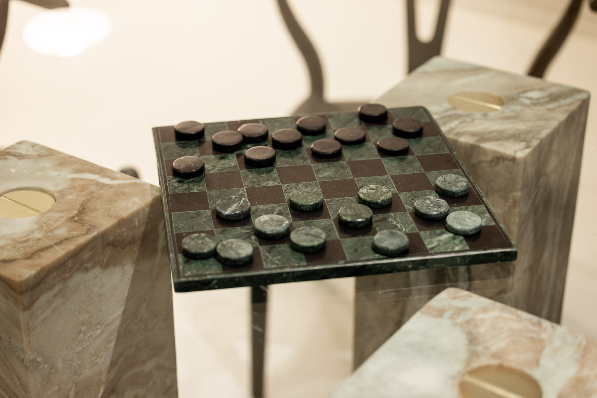Close-up view of a stylish green and black marble checkerboard game set, with matching marble pieces, resting on a unique stone pedestal. The intricate details of the game board are highlighted.