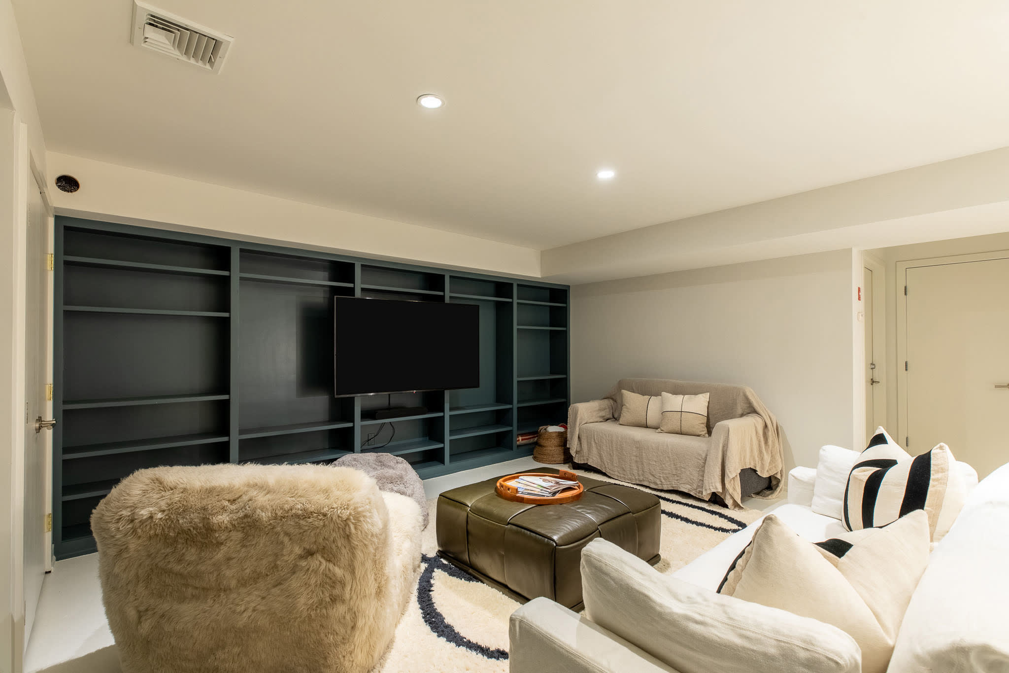 Inviting living space with a large flat-screen TV mounted within a dark teal built-in bookshelf, flanked by a white sofa and a plush, shaggy armchair. A small, neutral-colored sofa is also visible, creating multiple seating options.