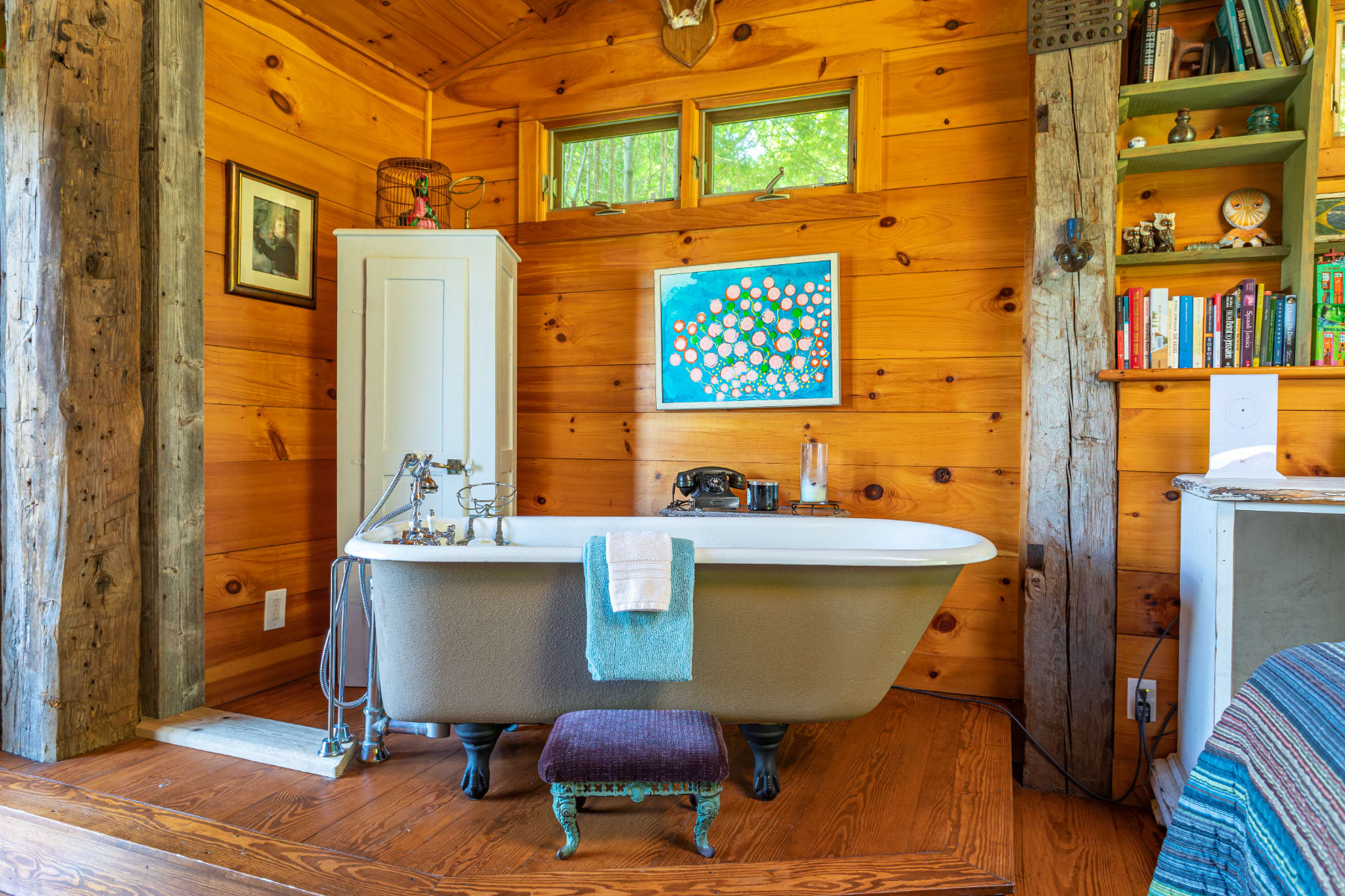 Close-up view of the elegant freestanding clawfoot bathtub, set on a raised wooden platform within the wood-paneled bedroom, complete with vintage-style fixtures and a small stool.