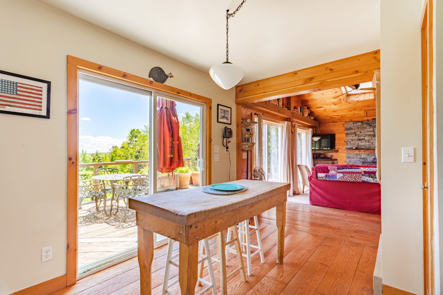 Kitchen area with a rustic wooden island and stools, featuring a large sliding glass door that opens to a deck with outdoor seating, and a glimpse of the living room with a red sofa.