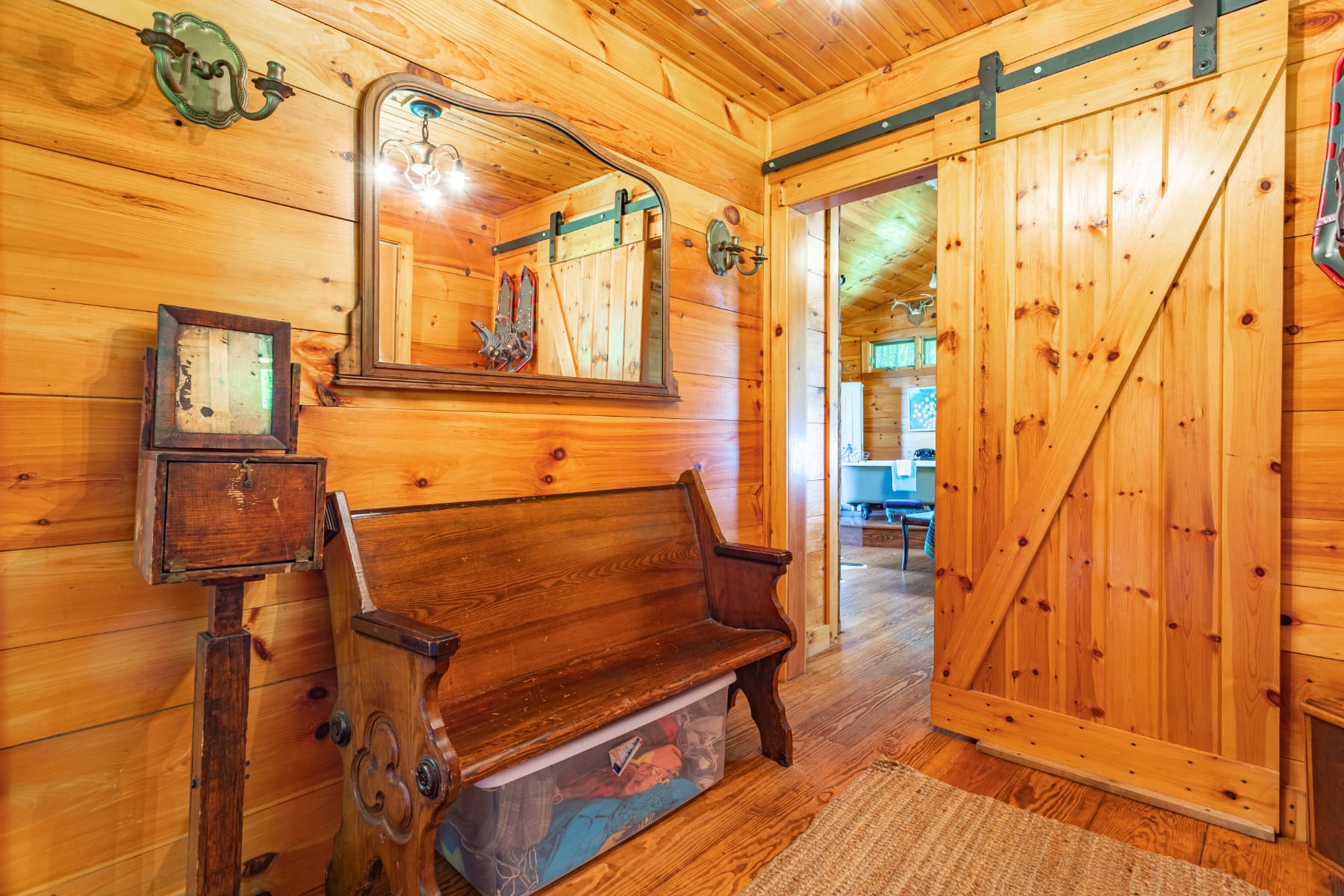 Inviting hallway or foyer with warm wood-paneled walls, featuring a rustic wooden church pew bench and a sliding barn door, leading to another room.