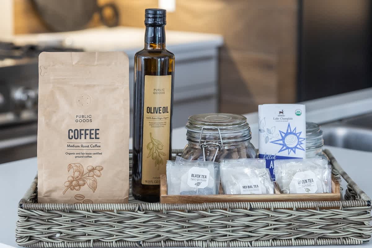 A thoughtful welcome basket on a kitchen counter contains coffee, olive oil, various tea bags, and a glass jar, providing essential amenities for guests.