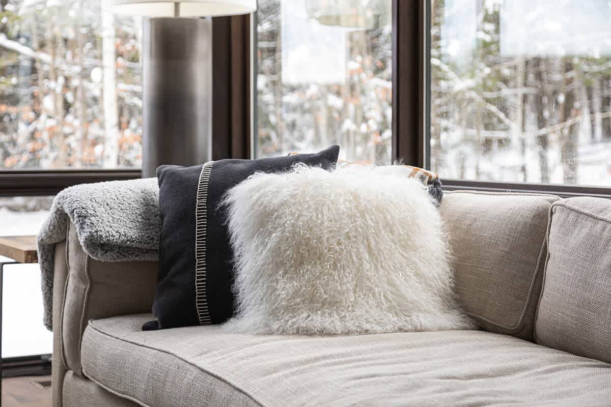 A close-up of a light-colored sofa adorned with decorative pillows, including a black one with white stitching and a fluffy white one, complemented by a cozy throw blanket.