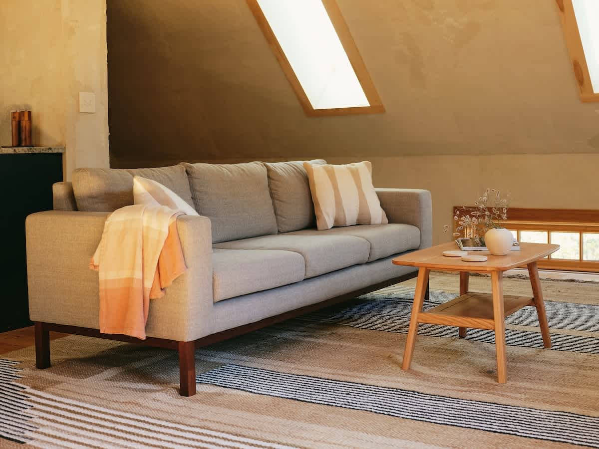 A comfortable living room showcases a light gray sofa adorned with throw pillows and a blanket, a wooden coffee table, and a striped rug. Hardwood floors and sloped ceilings complete the inviting space.