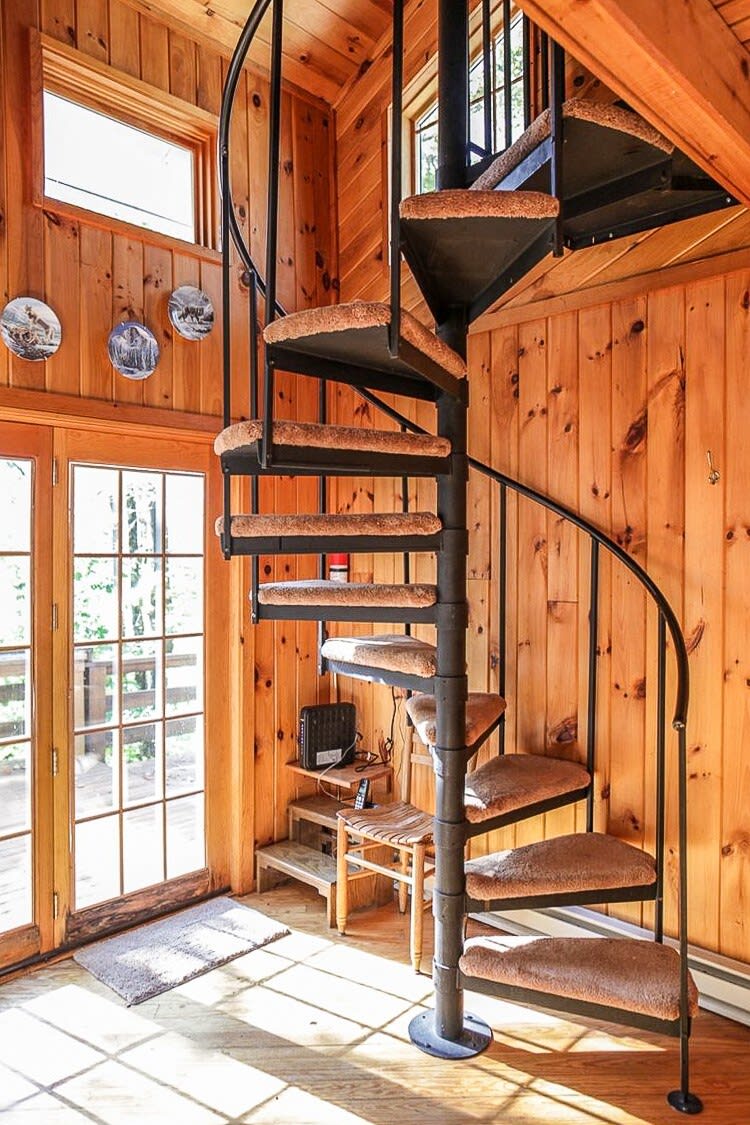 A striking black metal spiral staircase with carpeted treads dominates this wood-paneled space, leading upstairs. French doors with large glass panes open to an outdoor area, letting in natural light.