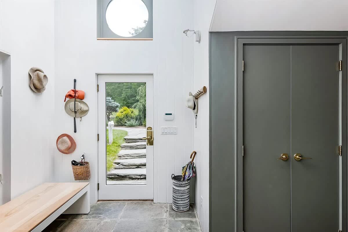 Modern entryway with slate tile flooring, a glass-paned entrance door, a built-in bench, and coat hooks, featuring a high ceiling with a round window above the door.