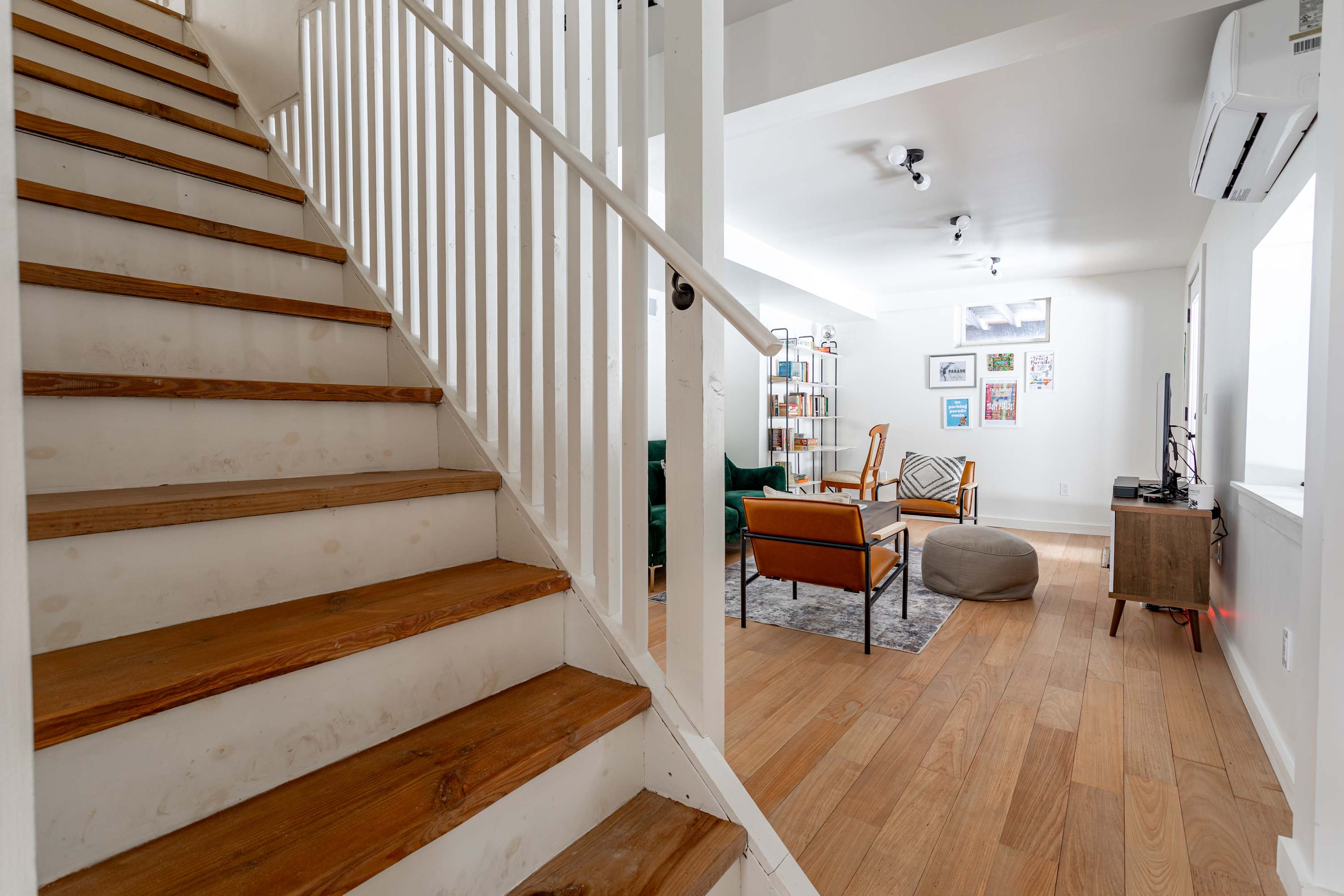 A wooden staircase with white risers and banister descends into a bright living space with light hardwood floors and modern furniture, creating an inviting transition area.