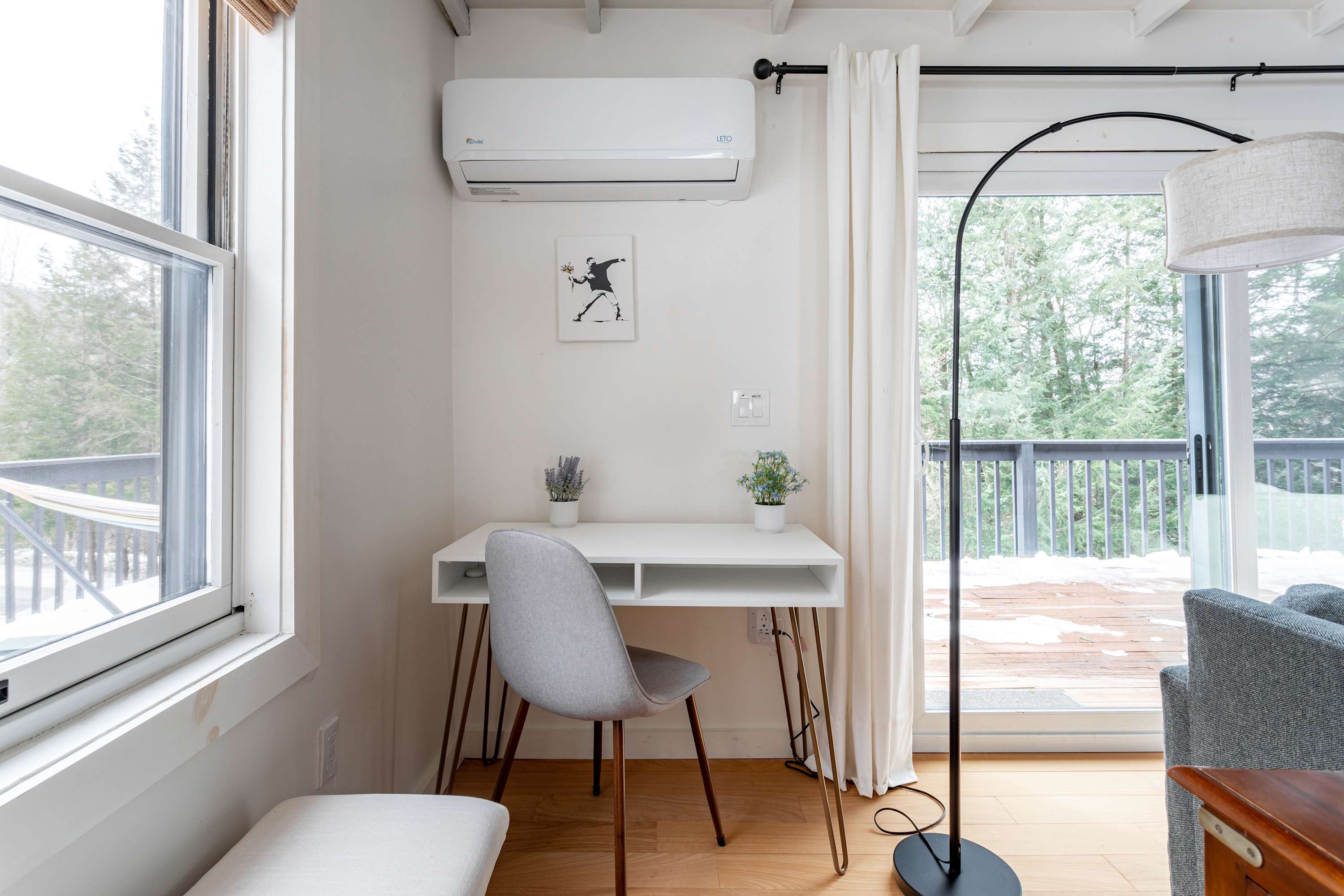 Dedicated workspace with a white desk and a grey chair, positioned by a large window and a sliding glass door, offering natural light and outdoor views. An air conditioning unit is mounted above.