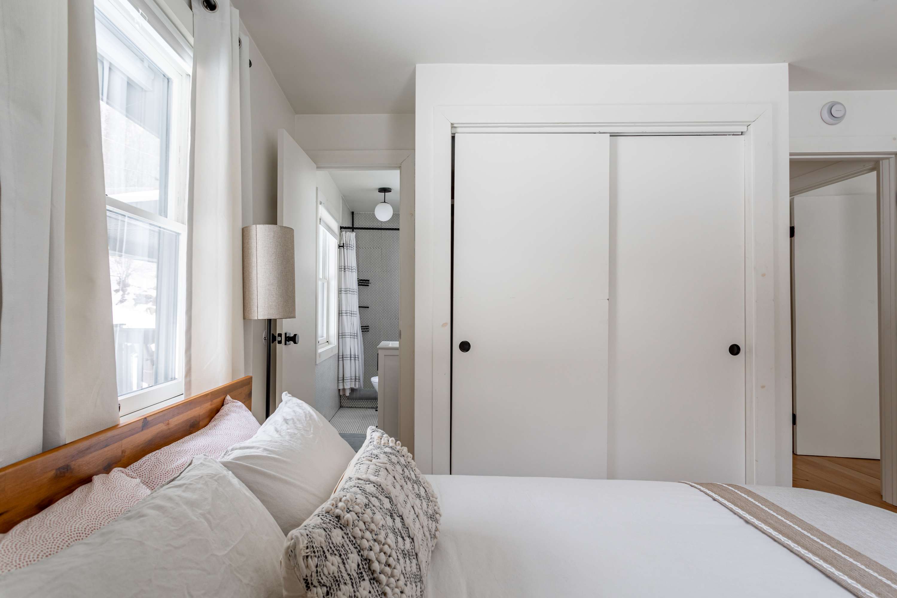 View of bedroom-1 showing a large closet with sliding doors and an open doorway leading to an en-suite bathroom. The room maintains a bright and clean aesthetic with white walls and hardwood floors.