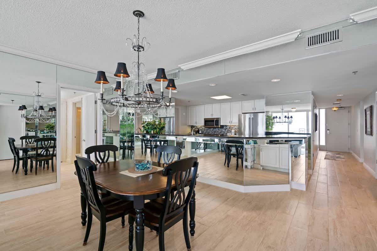 An open-concept dining area flows into the kitchen, featuring a dark wood dining table and a large mirrored kitchen island with black countertops. Mirrored walls throughout amplify the light and space.