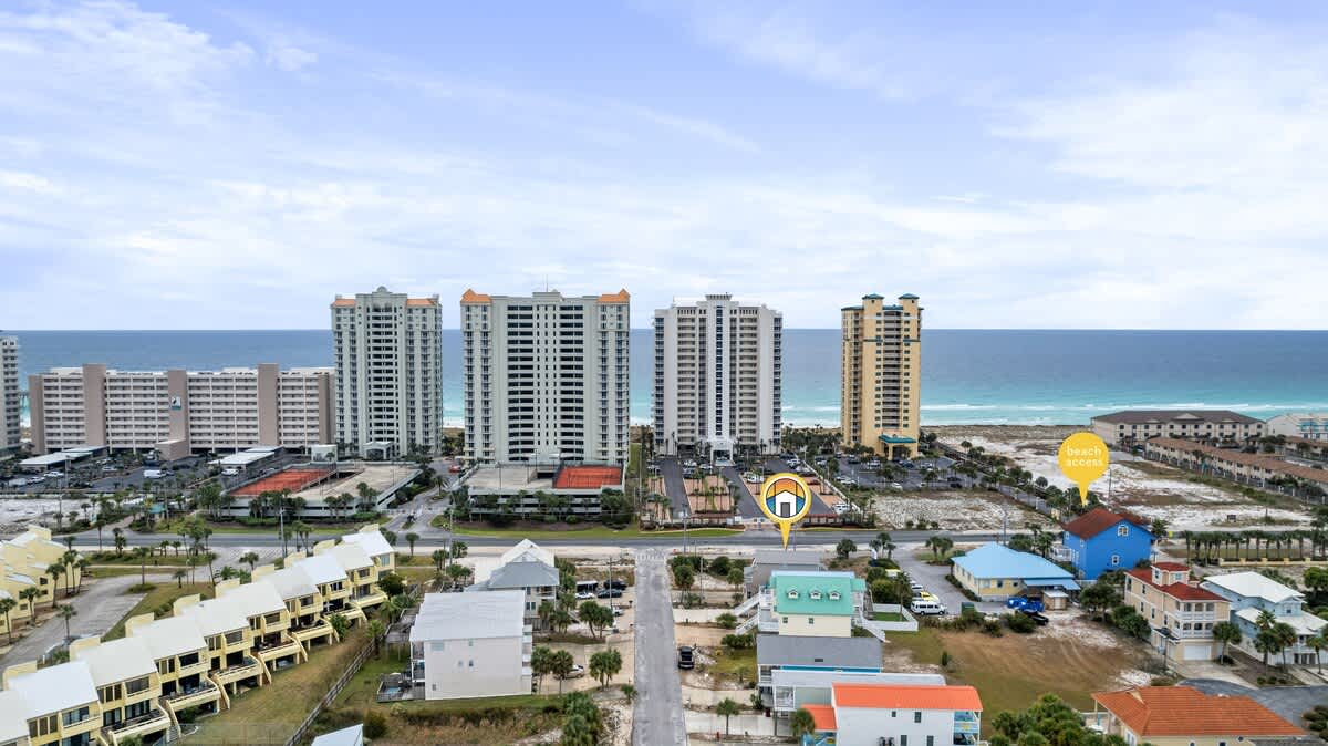 An aerial view showcases the property, marked with a house icon, situated on a street with other colorful houses, with the ocean and several high-rise buildings visible in the background, and a 'beach access' pin nearby.