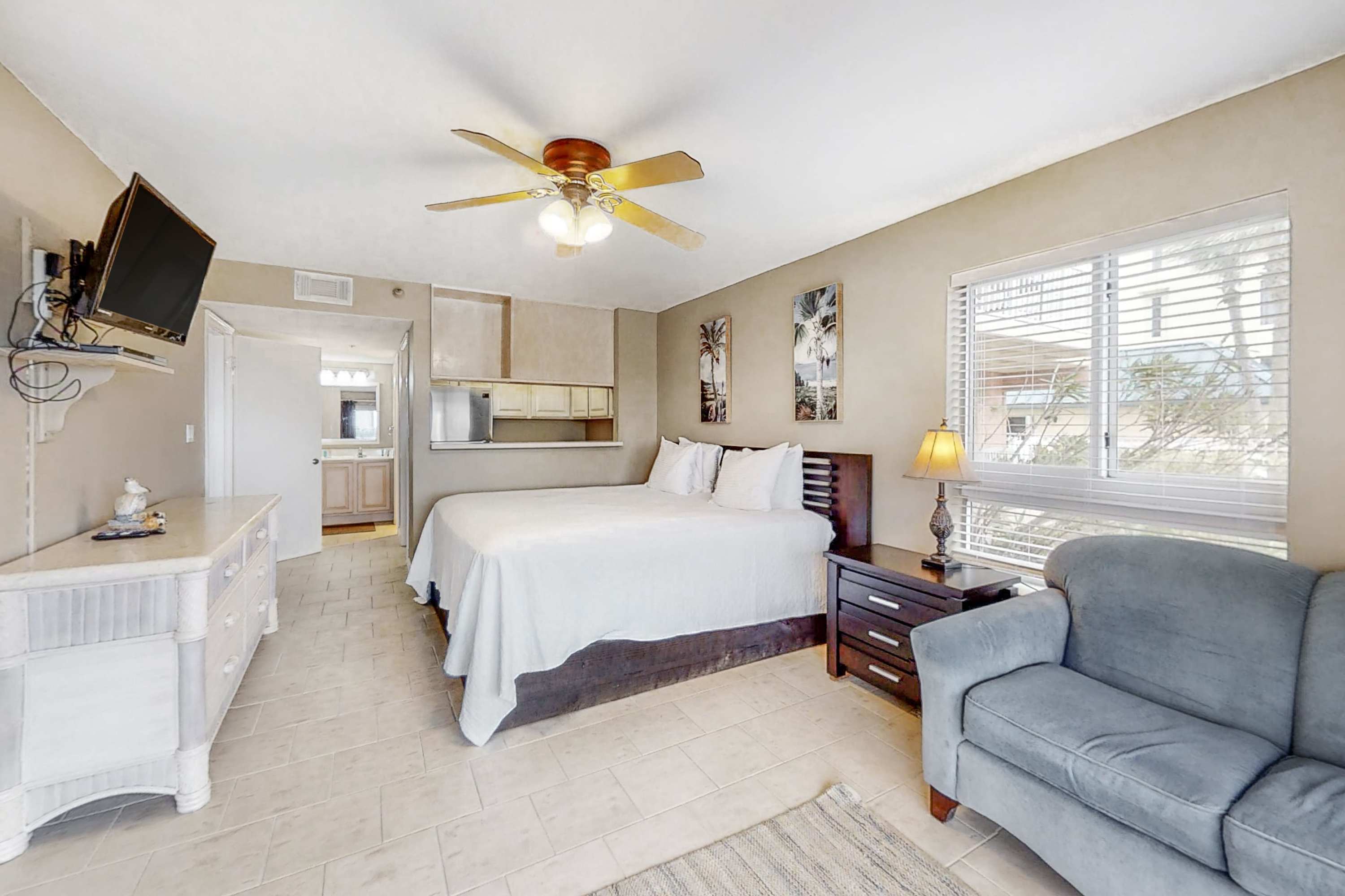 Another view of bedroom-2, showing the large bed, a light-colored dresser, a window with blinds, and a ceiling fan, all on light-colored tiled flooring.