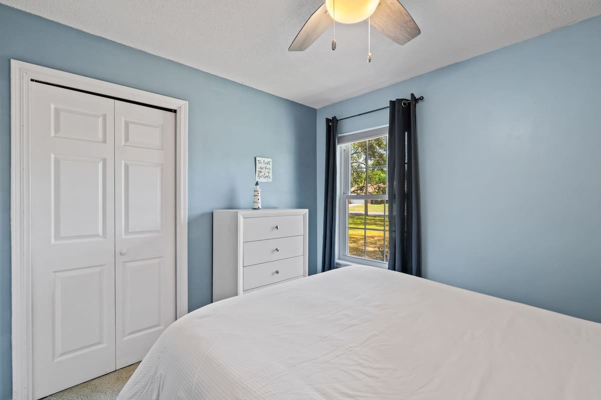 Another view of bedroom-3, showing a white dresser with three drawers, a white bi-fold closet door, and a window with dark blue curtains.