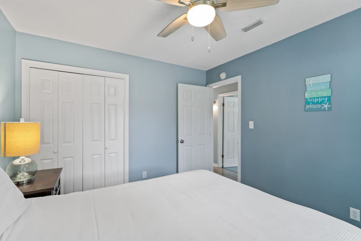 View of bedroom-1 showing a white bi-fold closet door, light blue walls, and a decorative 'Beach is my happy place' sign. A doorway leads to another room.