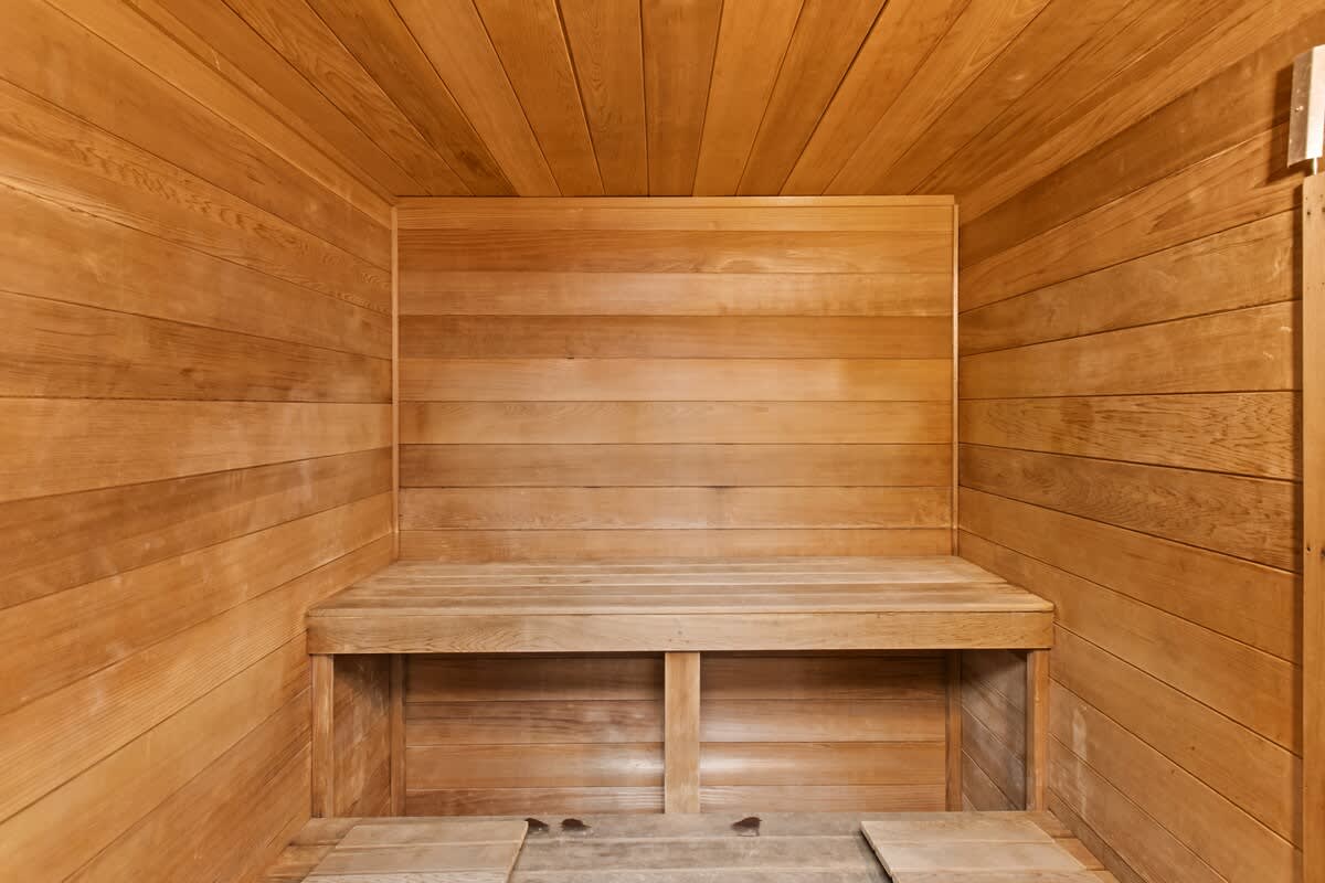 A cozy sauna room constructed entirely from light-colored wood planks, featuring a multi-tiered wooden bench for seating. The space is simple and designed for relaxation.