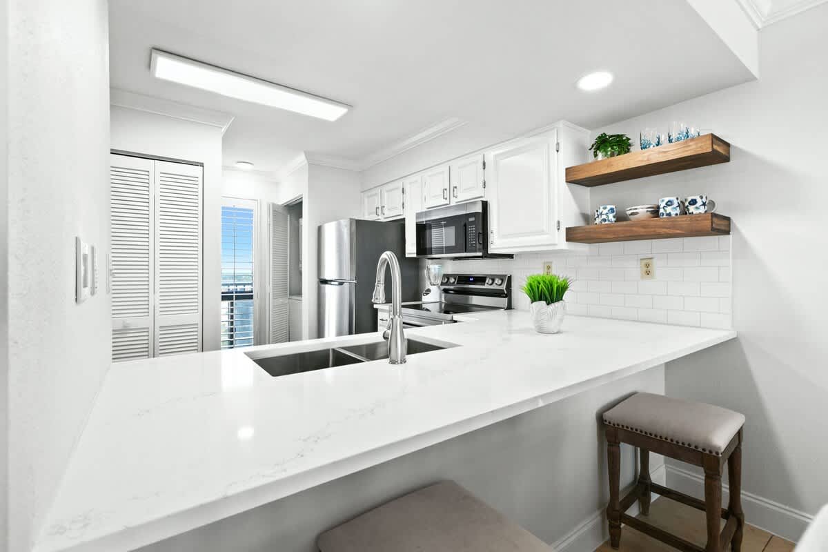 Modern kitchen featuring white shaker cabinets, a large white quartz countertop with an undermount double sink, stainless steel appliances, and a white subway tile backsplash.