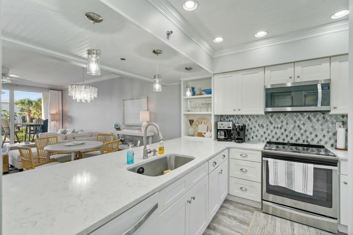 Bright and open kitchen with extensive white quartz countertops and white shaker cabinets, featuring a large sink and stainless steel appliances. The kitchen overlooks the dining and living areas, providing a seamless flow.