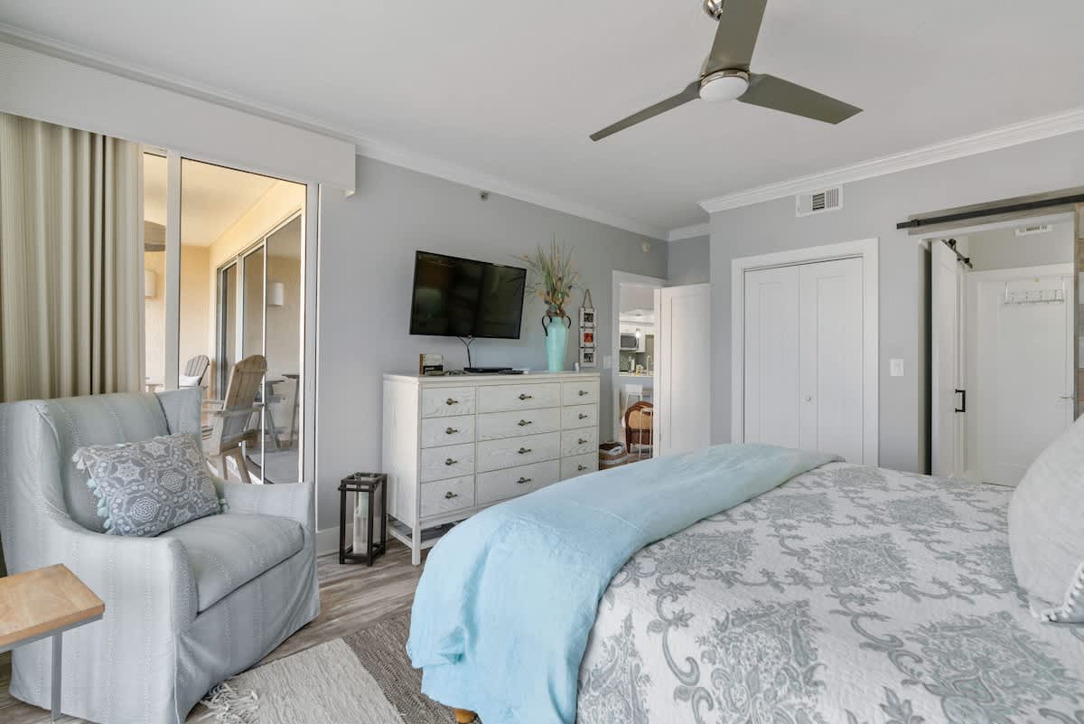 Coastal-themed bedroom with a king bed featuring a wicker headboard and light bedding, complemented by a sliding barn door revealing a modern en-suite bathroom.