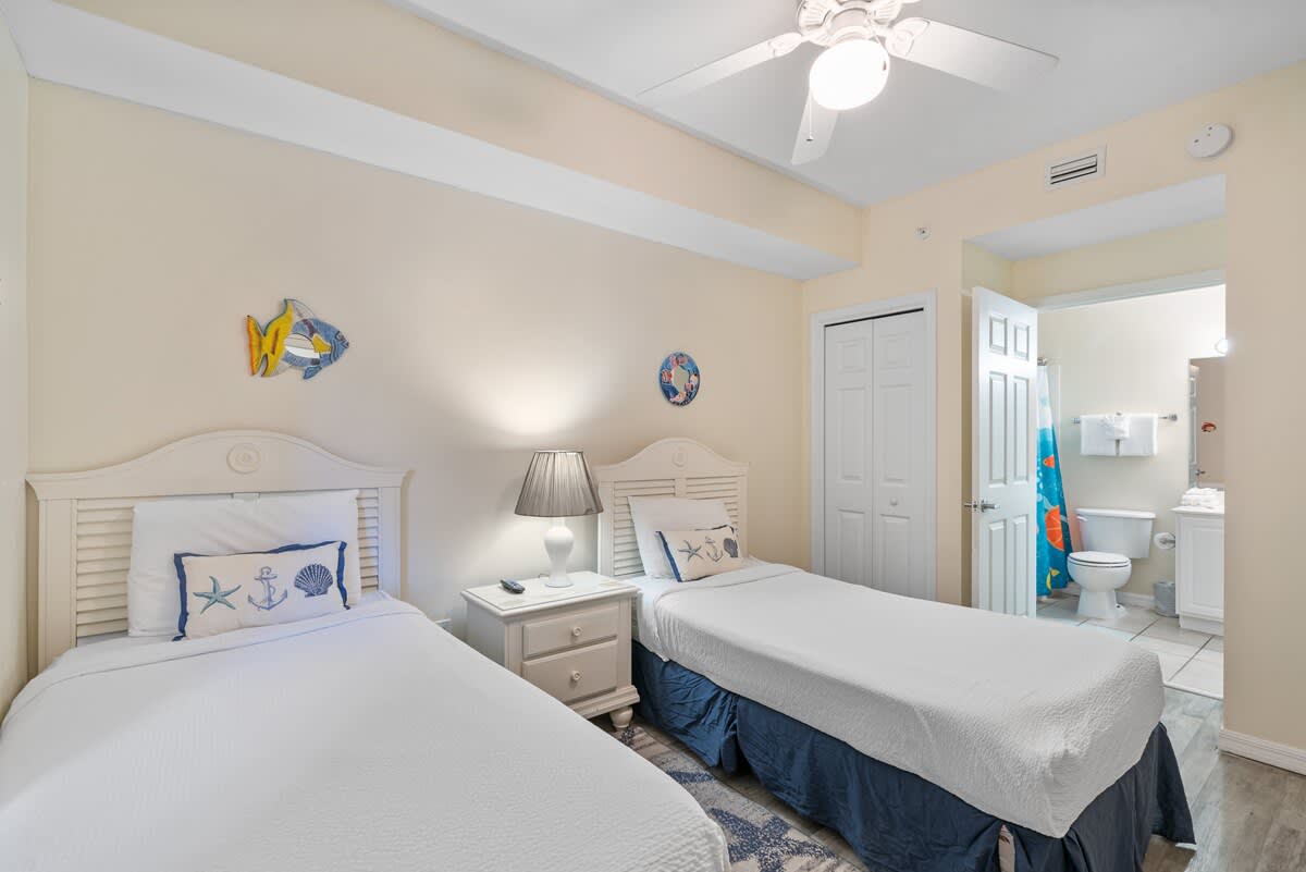Another angle of the twin bedroom, highlighting the two beds, a nightstand with a lamp, and an open doorway leading to an en-suite bathroom.