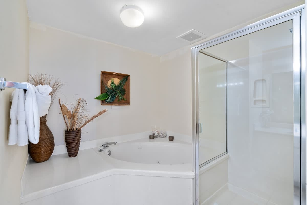 Bright bathroom featuring a corner jetted bathtub with chrome fixtures, a glass-enclosed shower, and light-colored walls, accented with decorative dried plants.