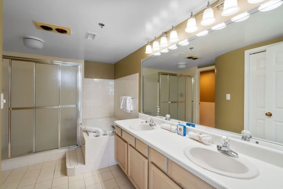 En-suite bathroom with a double vanity, light-colored tile flooring, and a shower/tub combination enclosed by a frosted glass sliding door. The walls are painted a warm tan color.