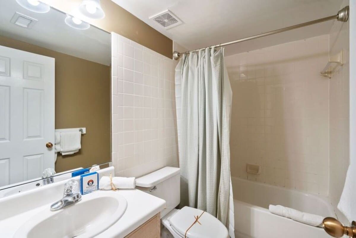 Full bathroom featuring a white toilet and a shower/bathtub combination with white subway tile surround and a light-colored shower curtain. The room has warm beige walls, a large mirror, and a vanity with a white countertop.