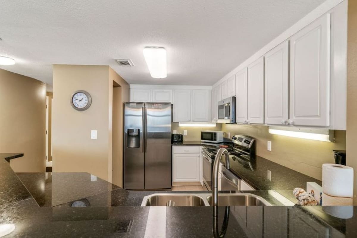 Well-equipped kitchen with stainless steel appliances including a side-by-side refrigerator, microwave, and electric range, complemented by white cabinetry and dark granite countertops.
