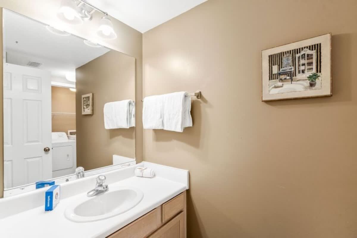 Bathroom with a single vanity featuring a white countertop, light wood cabinets, a large mirror with vanity lighting, and a towel rack with white towels.