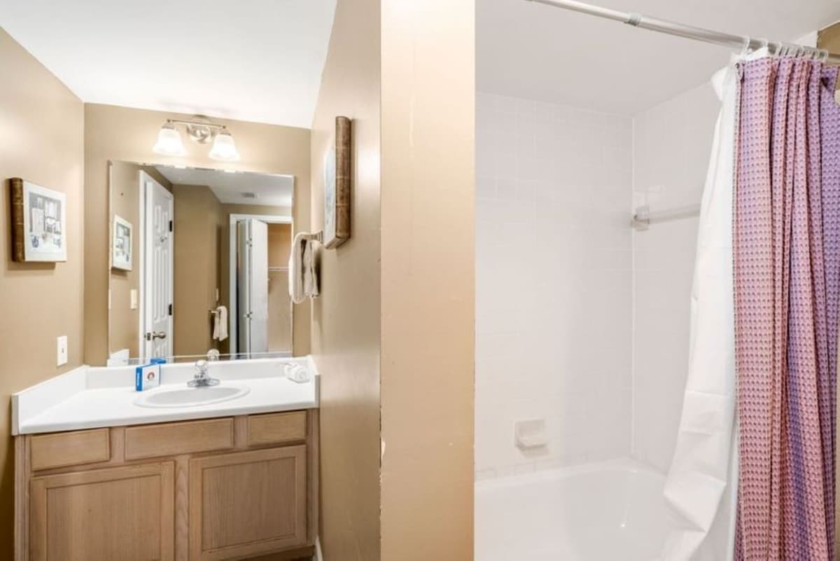 Bathroom featuring a single vanity with a white countertop and light wood cabinets, a mirror, and a shower/tub combination with a colorful shower curtain.