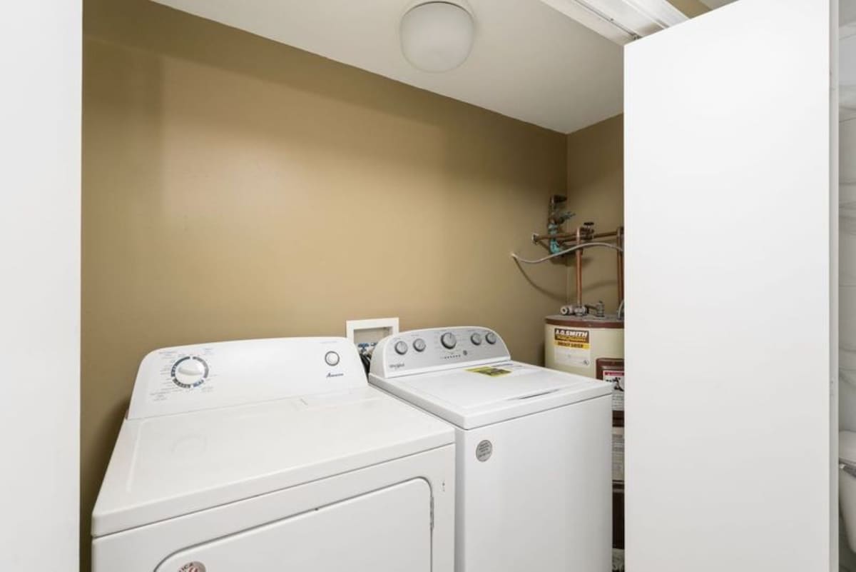 A dedicated laundry area featuring a white top-loading washing machine and a front-loading dryer. The space has warm beige walls and visible utility connections, indicating a functional and practical setup.