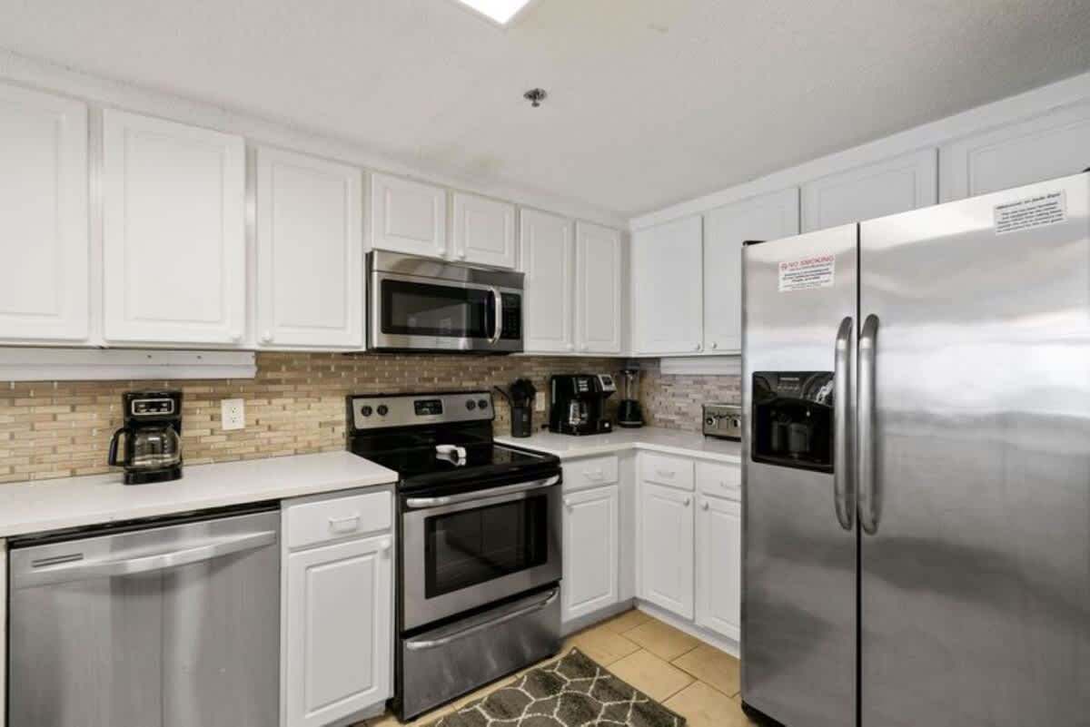 A detailed view of the kitchen appliances, including a stainless steel refrigerator, microwave, and electric range, set against white cabinetry and a mosaic tile backsplash.