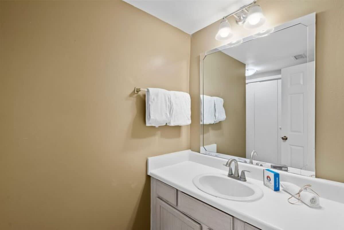 A bedroom wall with a light-colored, wicker-style dresser and a small wall-mounted television above it. Light wood-look flooring and a white door leading to another room are visible.