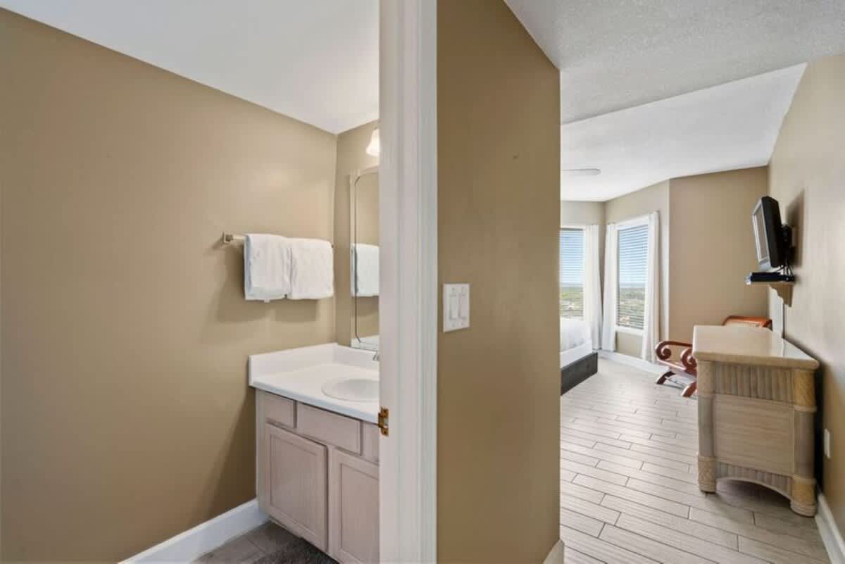 A bedroom featuring two queen-sized beds with crisp white bedding, a ceiling fan, and a large mirrored closet door reflecting the room. The walls are painted a warm tan.