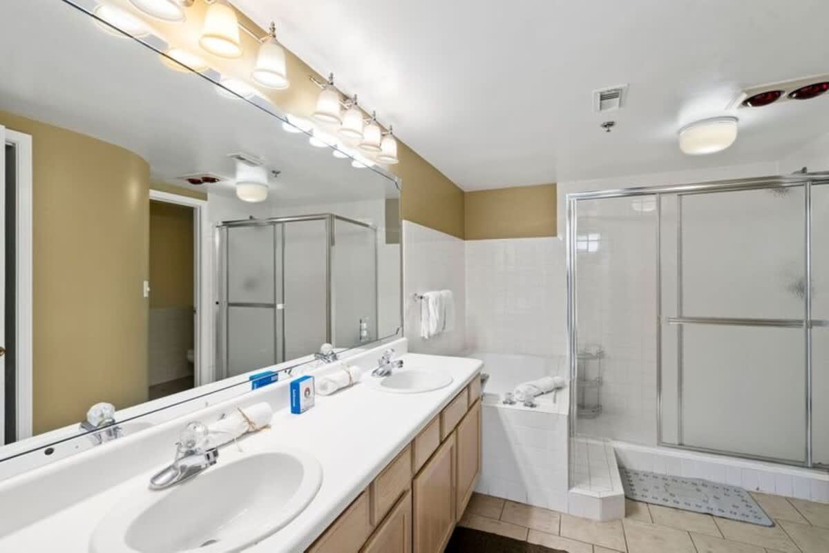 Another angle of the en-suite bathroom, highlighting the separate glass-enclosed shower next to the jetted bathtub. The double vanity with two sinks and a large mirror is also prominent.