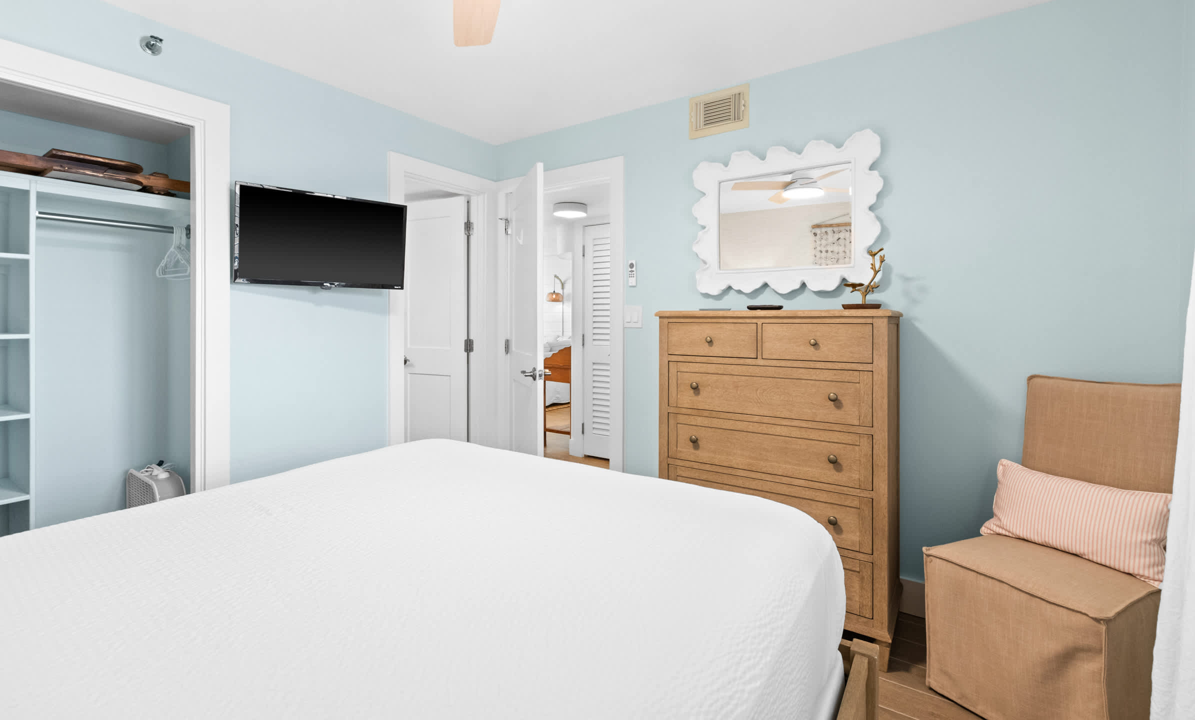 View of the guest bedroom showing a wooden dresser, a wall-mounted TV, and a mirror, with an open doorway leading to the hallway.