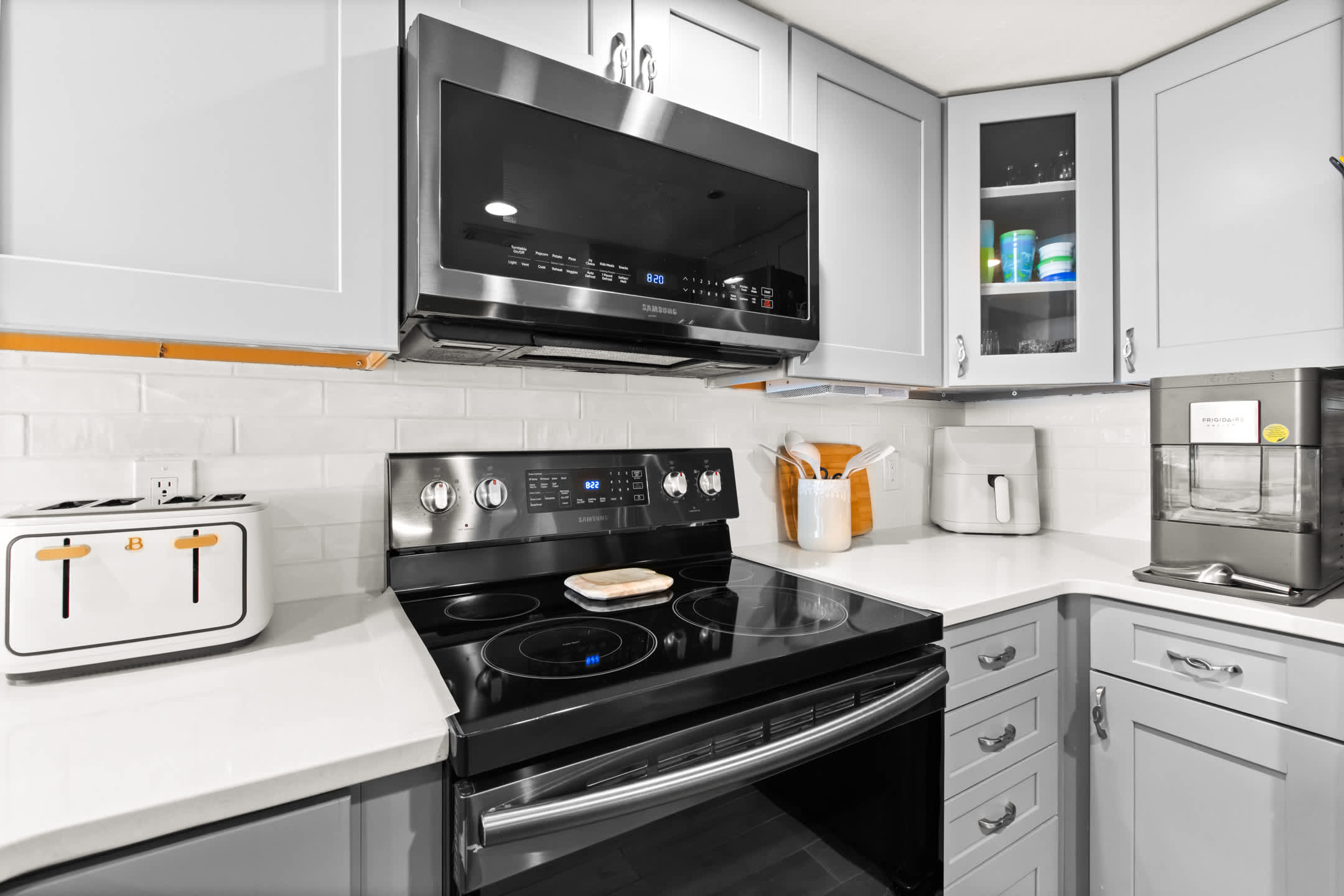 Close-up view of a modern kitchen featuring light gray cabinets, white subway tile backsplash, a black electric range with an overhead microwave, and various small appliances.