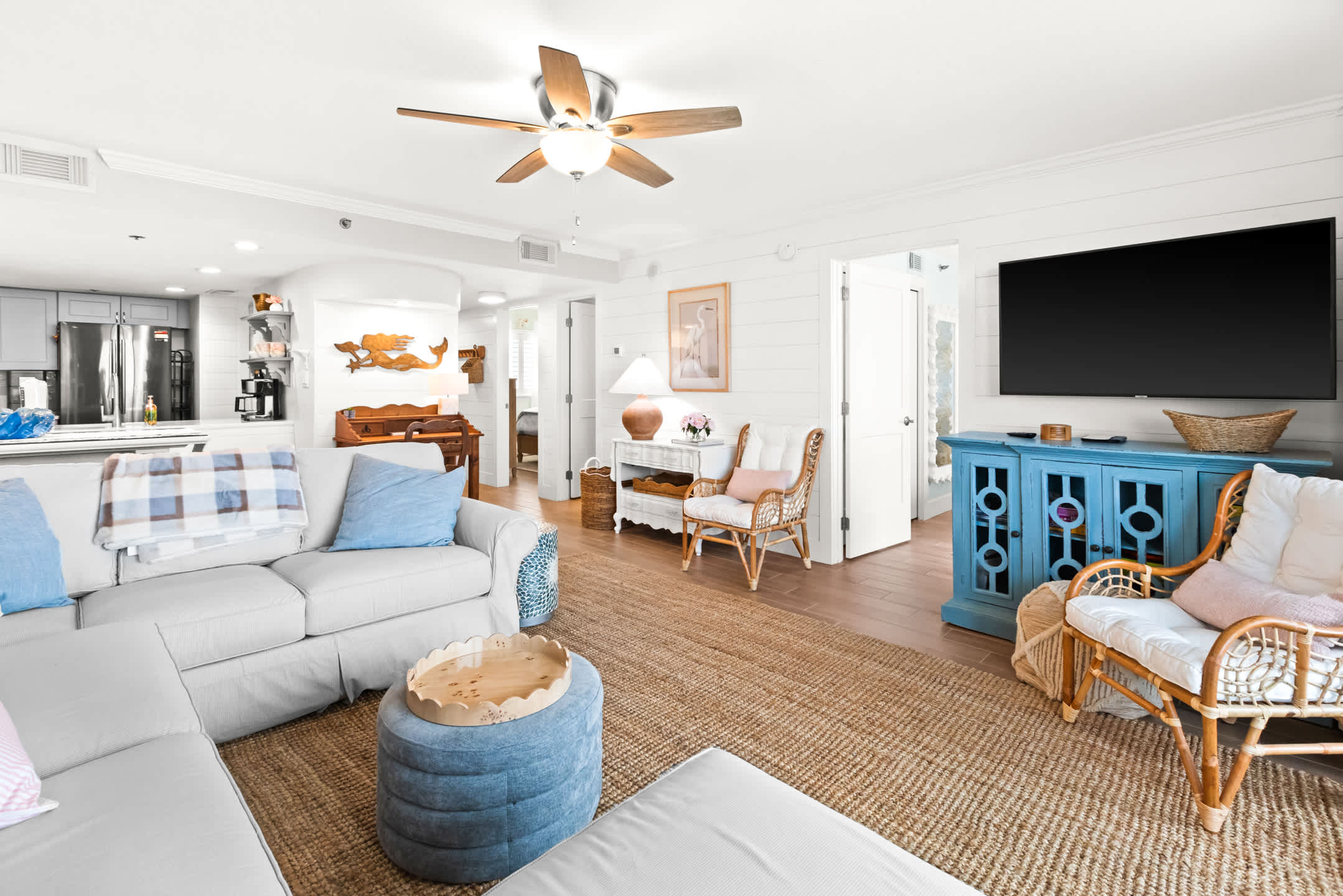 Inviting living room with a white slipcovered sectional, a vibrant blue console cabinet, and a view into the modern kitchen, featuring light wood flooring and shiplap walls.