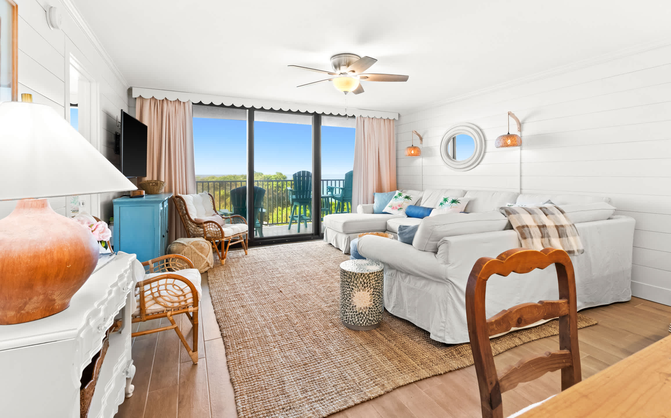 Bright and airy living room with a large white sectional, a jute rug, and a view of the balcony, featuring shiplap walls and an open doorway leading to an adjacent room.