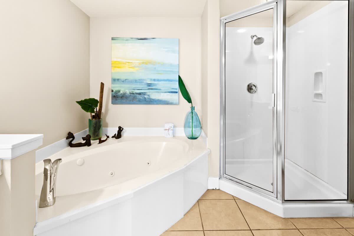A close-up of the bathroom's corner jetted tub and a glass-enclosed walk-in shower, accented with a vibrant piece of artwork and a large blue vase.