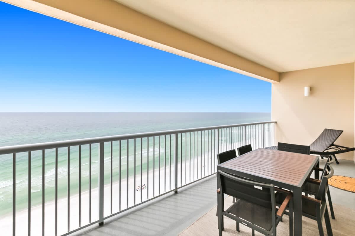 The wide balcony provides an unobstructed view of the ocean and beach, featuring an outdoor dining set and a lounge chair. The railing offers safety while enjoying the scenery.