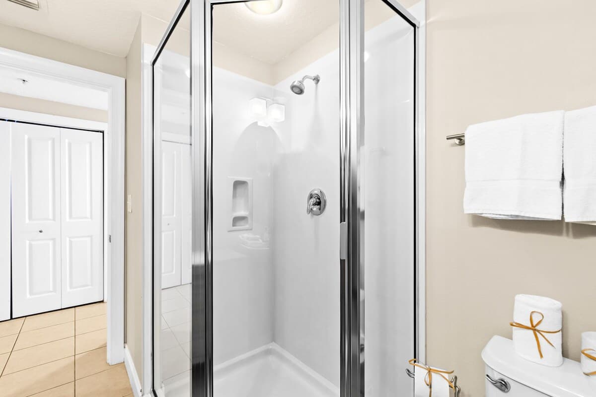A clean bathroom showcases a glass-enclosed walk-in shower with a white base and chrome fixtures. White towels are neatly folded on a rack next to the shower.