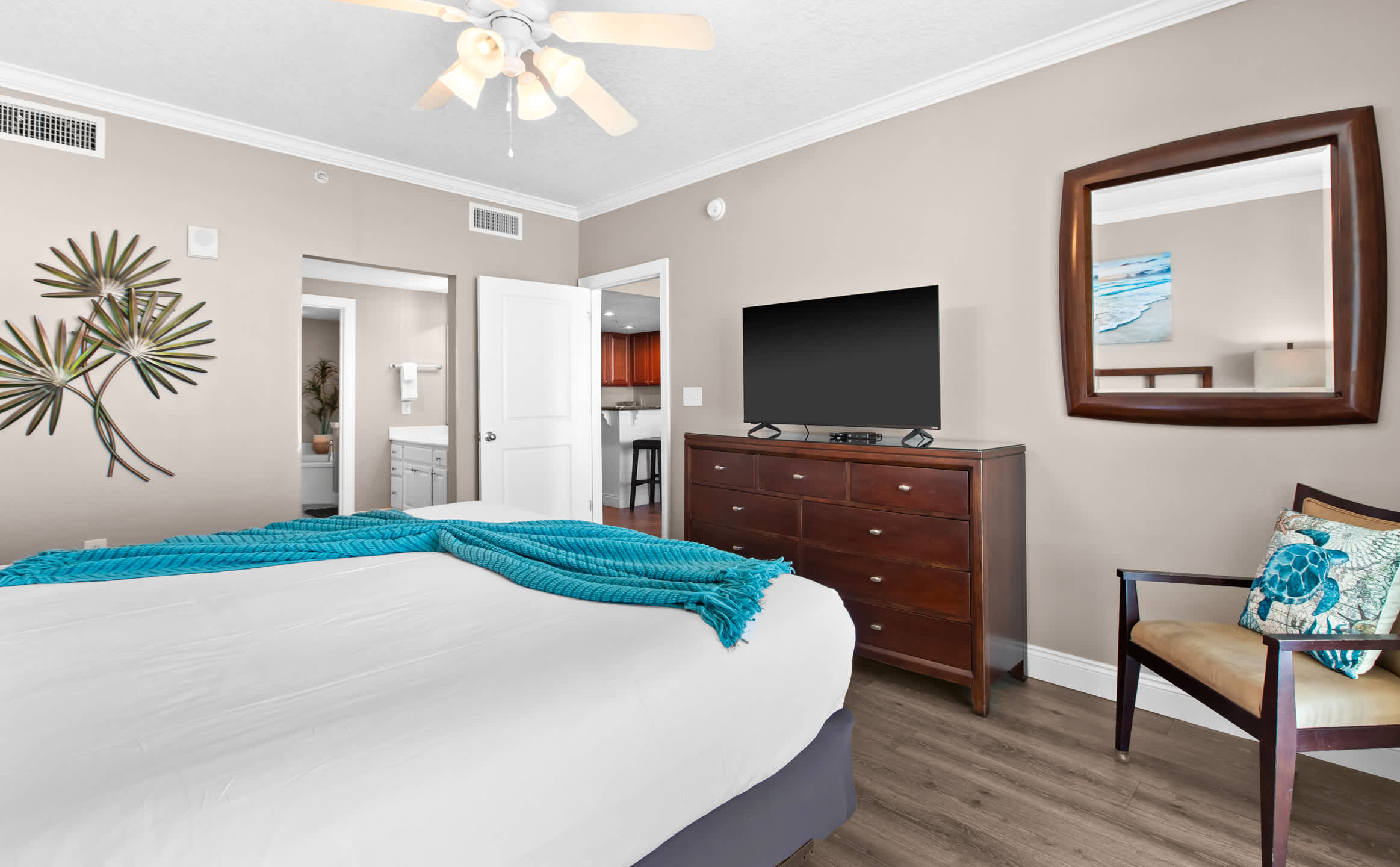 View of bedroom-2 showing the entrance to an ensuite bathroom, a large flat-screen TV on a dark wood dresser, and a decorative chair with a sea turtle pillow.