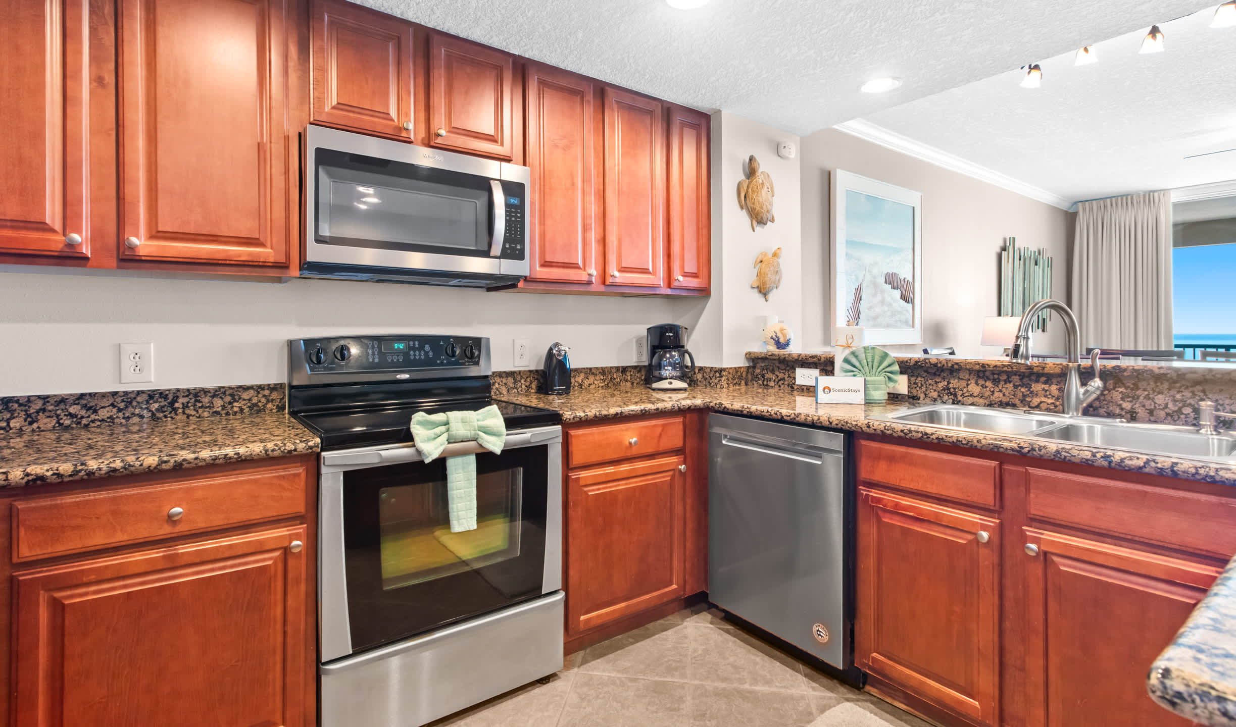 A functional kitchen showcases cherry wood cabinets, dark granite countertops, and stainless steel appliances, including a range with an overhead microwave, a dishwasher, and a double sink, with a decorative towel draped over the oven handle.