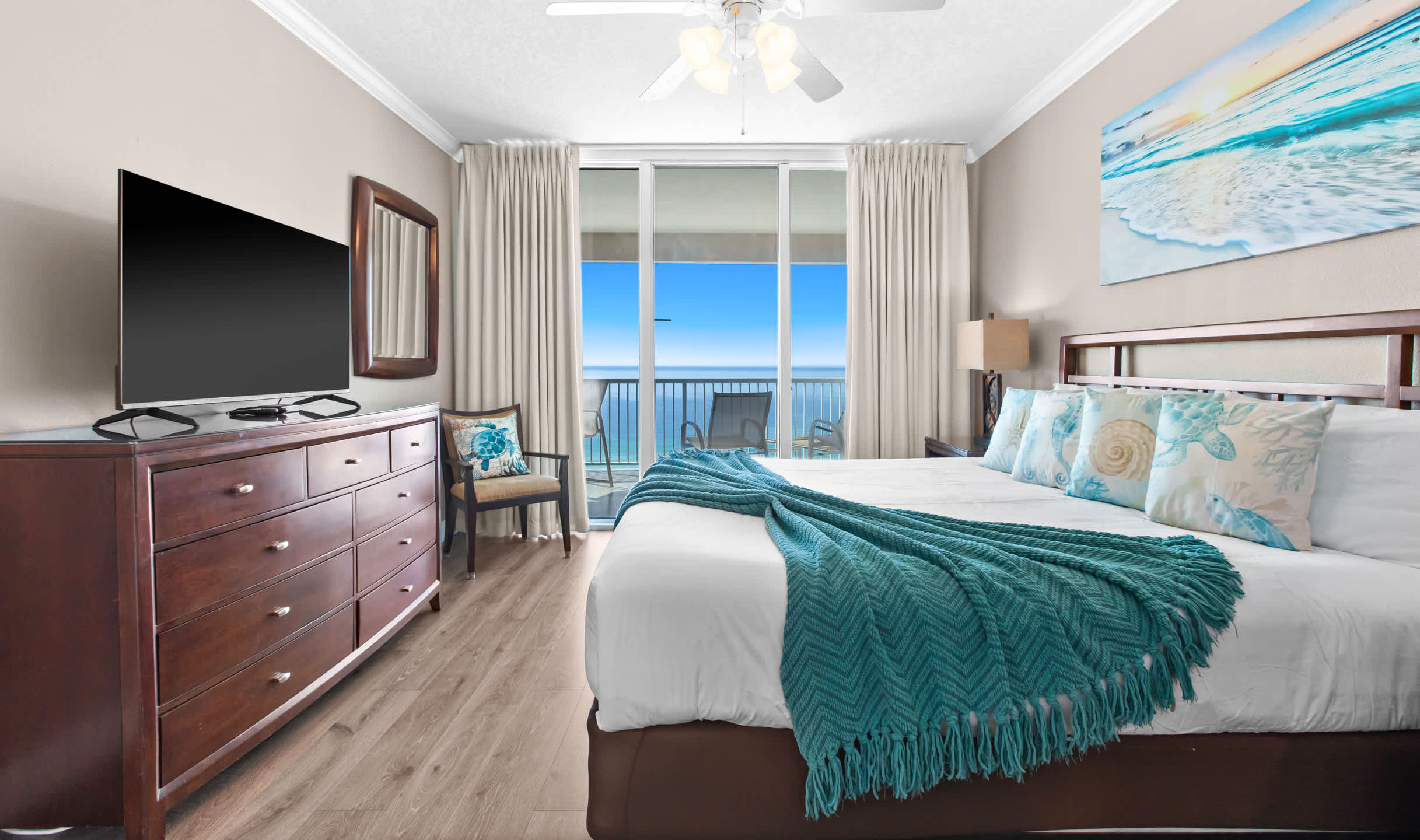 Another view of bedroom-2, highlighting a large flat-screen TV atop a dark wood dresser, a decorative chair, and the expansive ocean view from the private balcony.