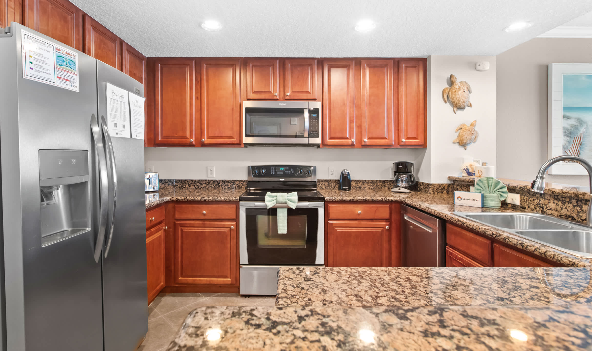 This modern kitchen boasts warm wooden cabinets, speckled granite countertops, and stainless steel appliances including an oven/stove, microwave, and dishwasher, with a double sink and coffee maker visible.
