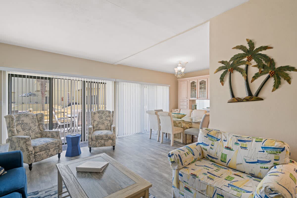 A wide view of the living and dining area, featuring a blue sofa, various armchairs, a dining table with white chairs, and sliding glass doors leading to an outdoor space.