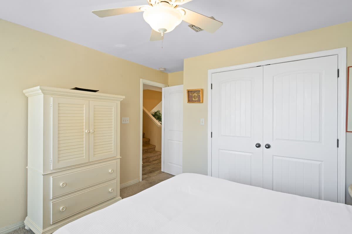 A corner of Bedroom 1 shows a white armoire and a closet with white paneled doors, with a doorway leading to a hallway and stairs, all under a ceiling fan.