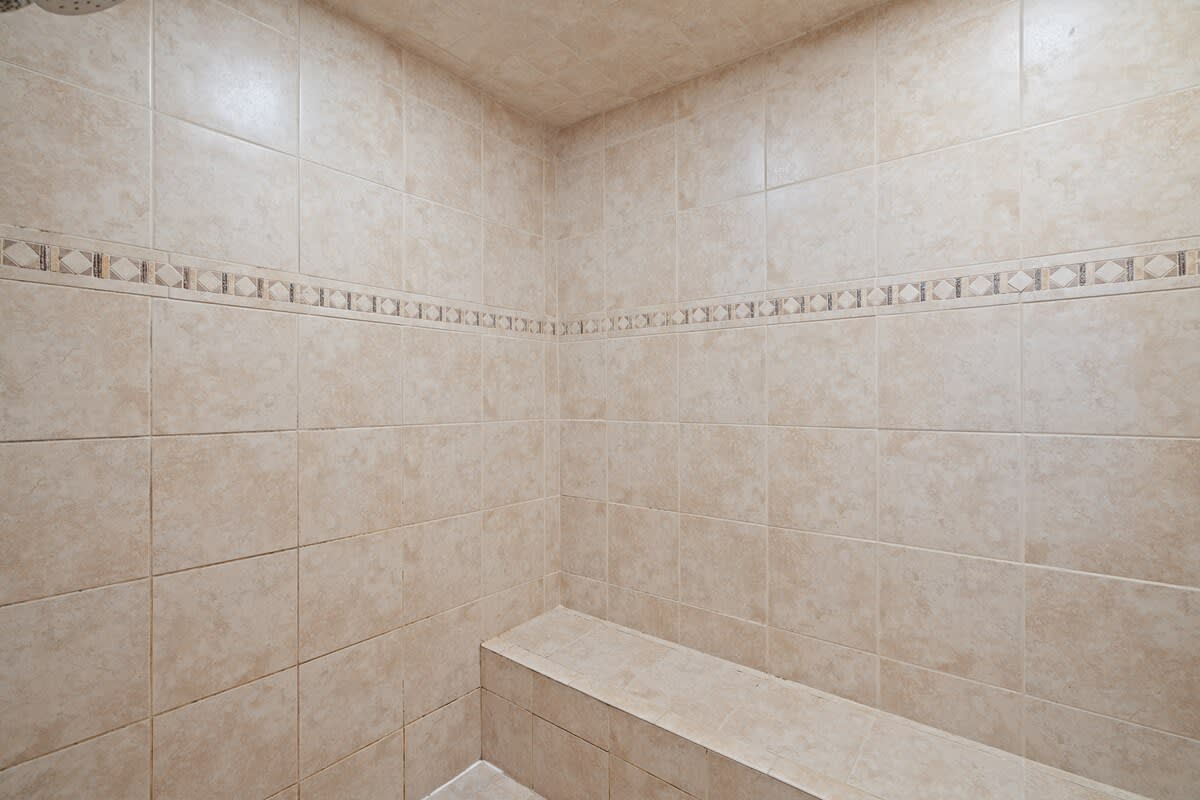 Tiled shower stall with light beige tiles, a decorative border, and a built-in bench, providing a functional and clean bathing space.